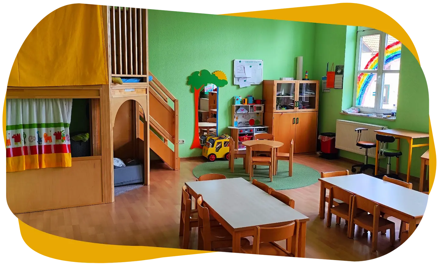 Gruppenraum der Grünen Gruppe mit Spielbereichen, Kindertischen und Spielecke