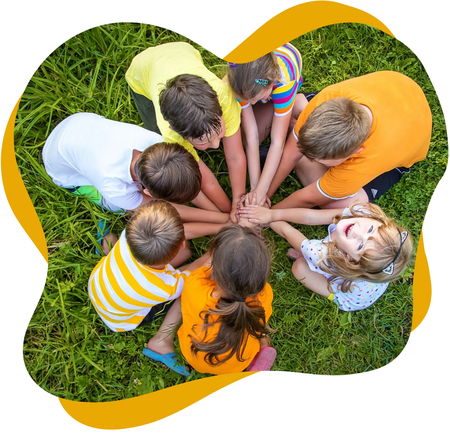 Kinder sitzen im Kreis auf einer Wiese und legen gemeinsam ihre Hände in die Mitte