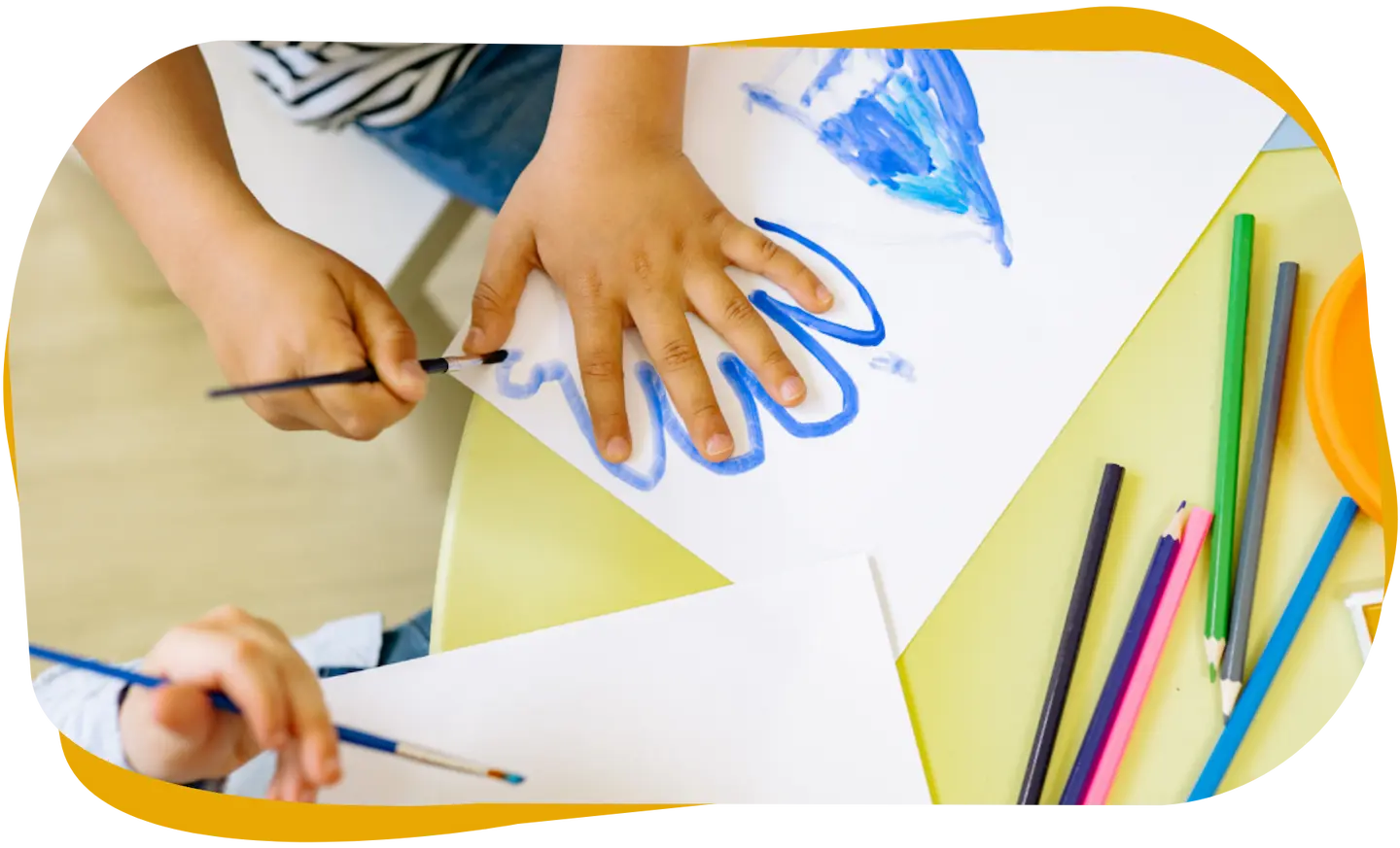 Kinder malen mit Pinseln auf Papier an einem Tisch